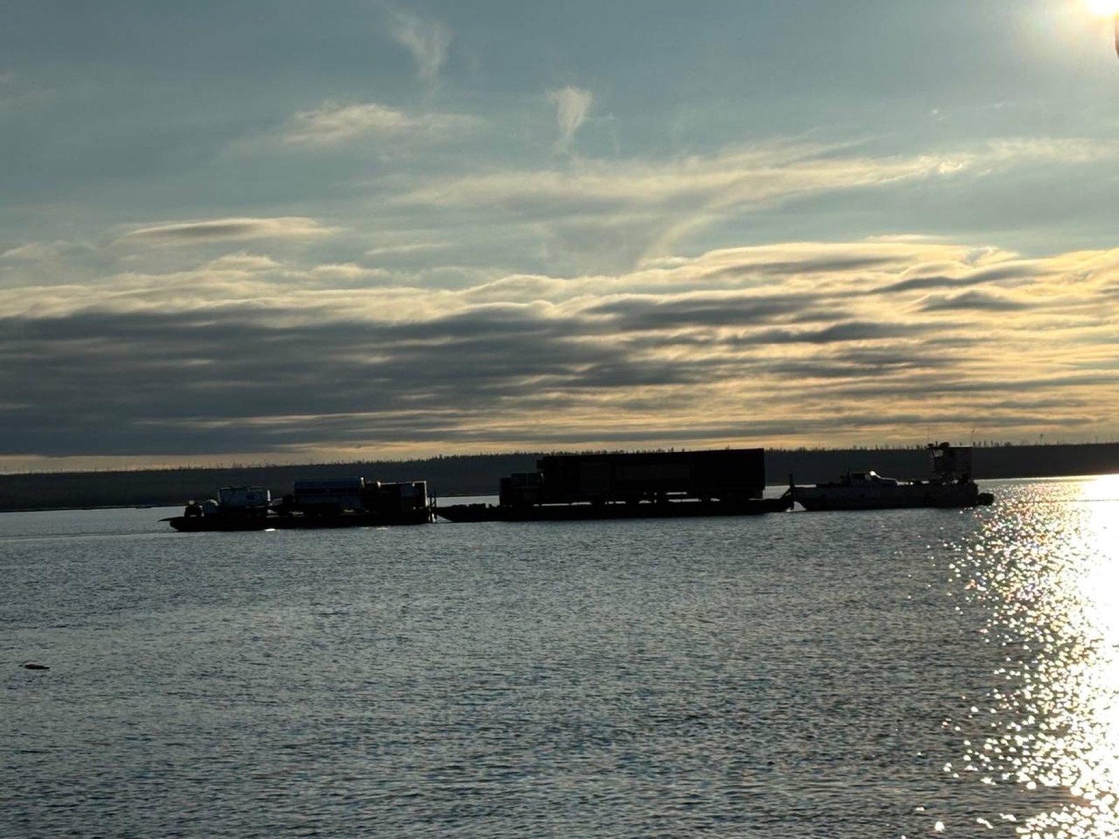 P&M Barging vessel hauling heavy equipment across Lake Athabasca at golden hour